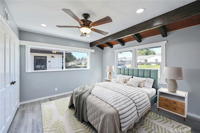 bedroom featuring ceiling fan, multiple windows, hardwood / wood-style floors, and vaulted ceiling with beams