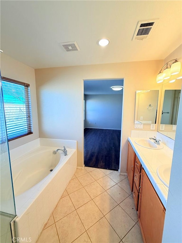 bathroom with tile patterned flooring, vanity, and a relaxing tiled tub