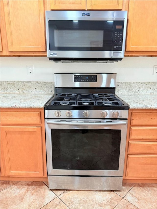 kitchen with light tile patterned flooring, stainless steel appliances, and light stone countertops