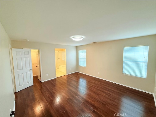 unfurnished bedroom with a walk in closet, connected bathroom, dark hardwood / wood-style flooring, and a closet