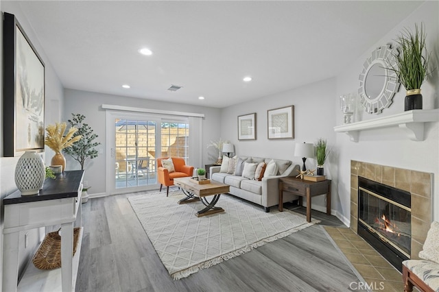 living area with a tile fireplace, wood finished floors, baseboards, visible vents, and recessed lighting