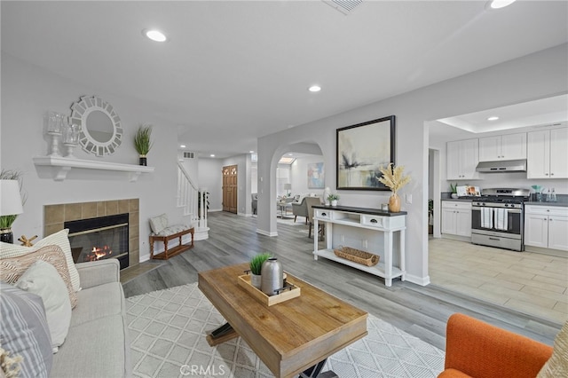 living area with light wood finished floors, stairway, recessed lighting, a tiled fireplace, and arched walkways