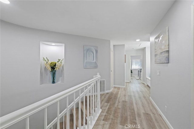 corridor featuring light wood-style floors, an upstairs landing, baseboards, and attic access