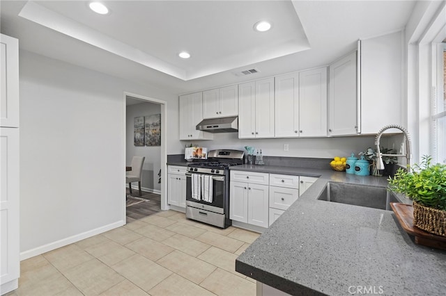 kitchen featuring white cabinetry, a tray ceiling, stainless steel range with gas stovetop, under cabinet range hood, and a sink