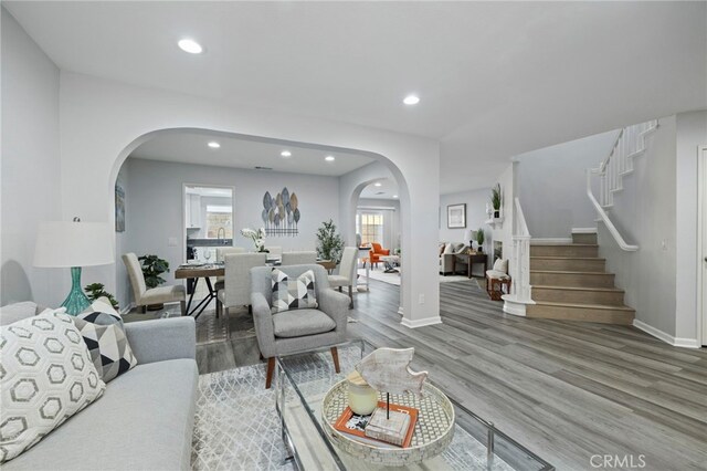 living room featuring stairs, recessed lighting, baseboards, arched walkways, and wood finished floors