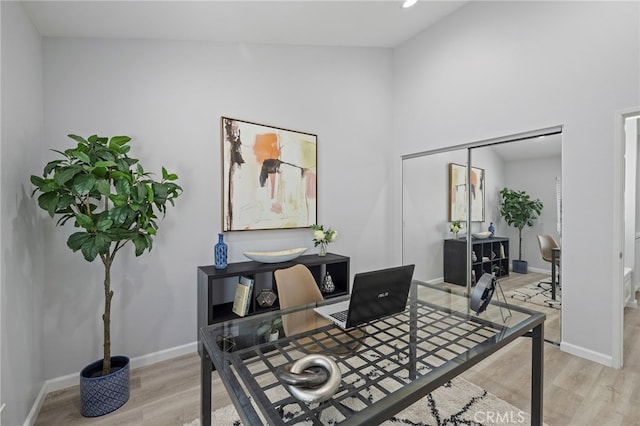 home office featuring a towering ceiling, baseboards, and light wood-type flooring