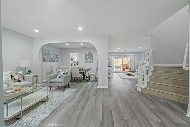 living room with recessed lighting, wood finished floors, arched walkways, and stairway