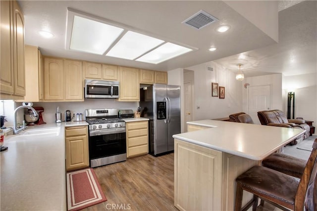 kitchen featuring hardwood / wood-style floors, appliances with stainless steel finishes, light brown cabinets, sink, and a breakfast bar