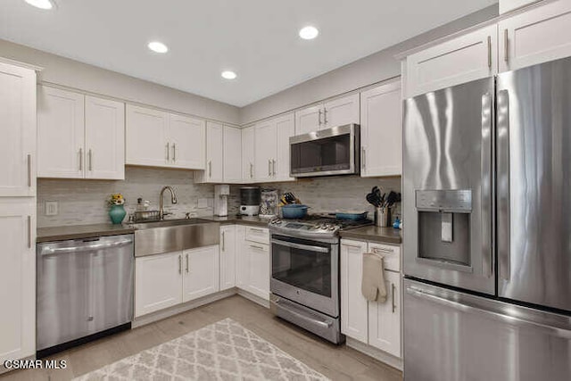 kitchen with white cabinets, appliances with stainless steel finishes, tasteful backsplash, light hardwood / wood-style floors, and sink