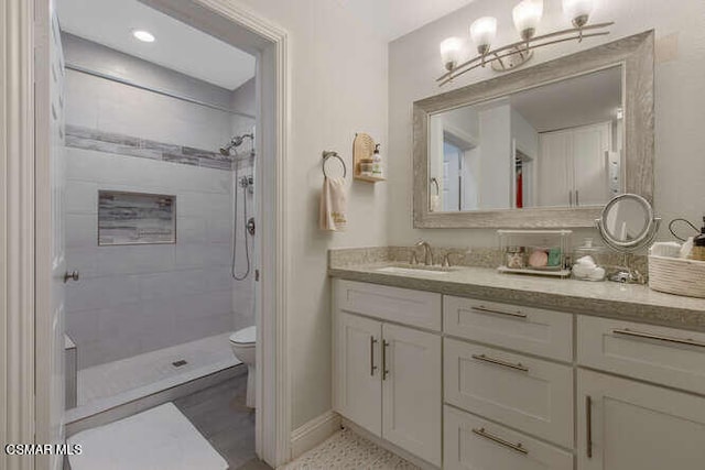 bathroom featuring toilet, a tile shower, and vanity