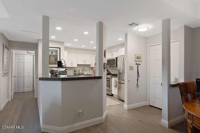 kitchen featuring kitchen peninsula, sink, white cabinetry, light hardwood / wood-style flooring, and stainless steel appliances