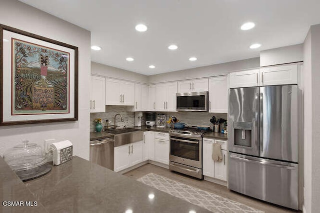 kitchen featuring tasteful backsplash, dark stone countertops, sink, stainless steel appliances, and white cabinets