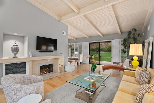 living room featuring vaulted ceiling with beams, wood-type flooring, and a tile fireplace