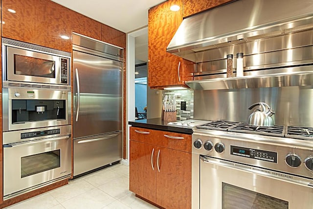 kitchen with backsplash, light tile patterned floors, extractor fan, and built in appliances