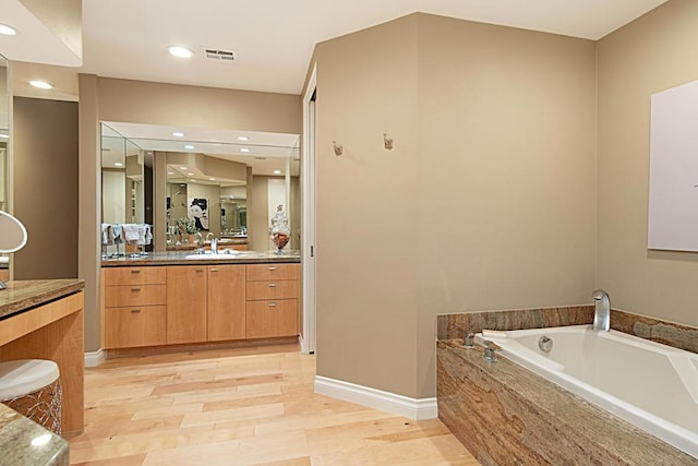 bathroom with hardwood / wood-style flooring, tiled tub, and vanity