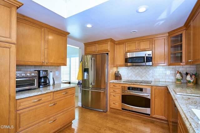 kitchen with tasteful backsplash, appliances with stainless steel finishes, light stone counters, and light hardwood / wood-style floors