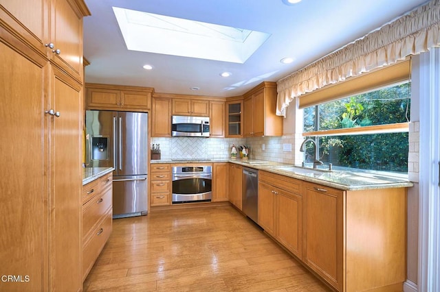 kitchen featuring sink, appliances with stainless steel finishes, a skylight, light stone counters, and light wood-type flooring