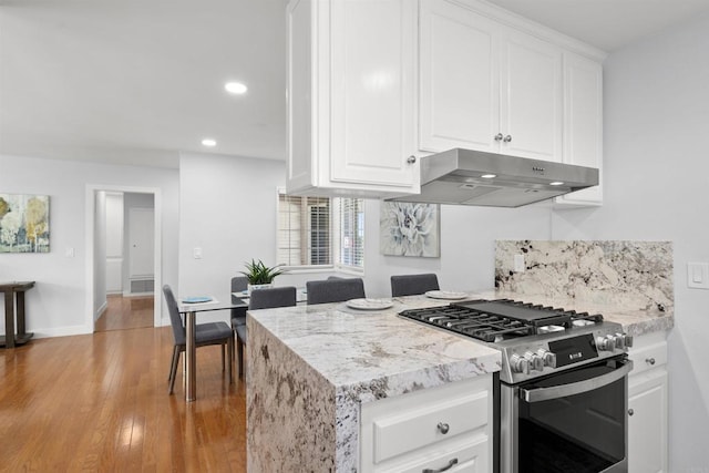 kitchen with light stone counters, white cabinetry, light wood-type flooring, and stainless steel gas range oven