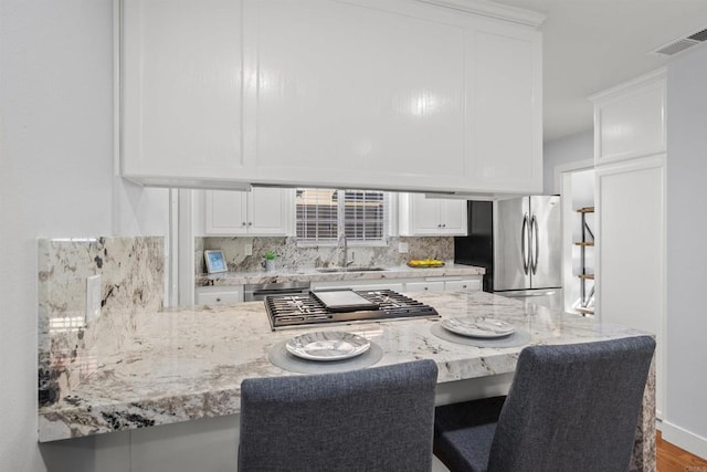 kitchen featuring white cabinetry, kitchen peninsula, appliances with stainless steel finishes, decorative backsplash, and sink