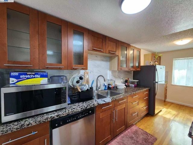 kitchen featuring appliances with stainless steel finishes, sink, light wood-type flooring, dark stone counters, and a textured ceiling