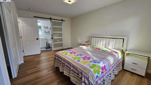 bedroom with wood-type flooring, a barn door, ensuite bathroom, and a textured ceiling