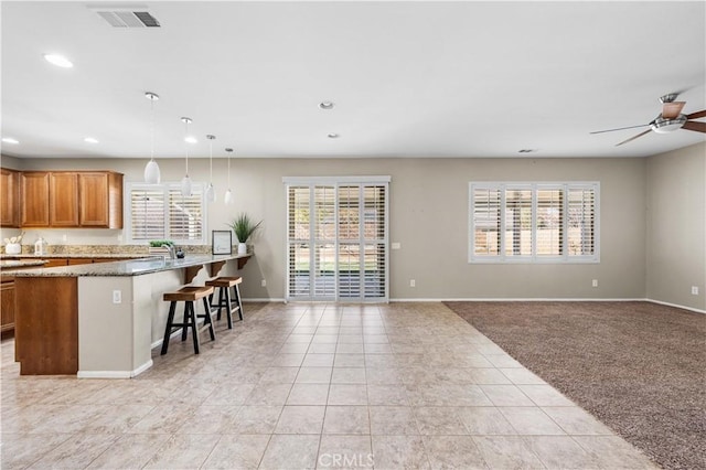 kitchen featuring ceiling fan, light colored carpet, pendant lighting, a breakfast bar area, and dark stone counters