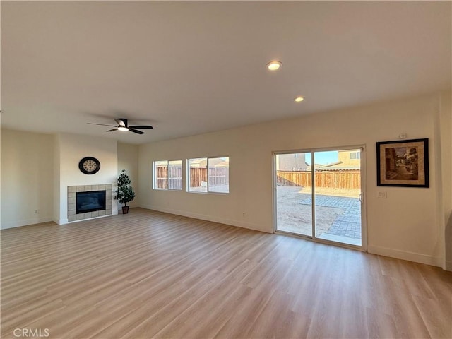 unfurnished living room featuring light hardwood / wood-style floors, a wealth of natural light, a tile fireplace, and ceiling fan