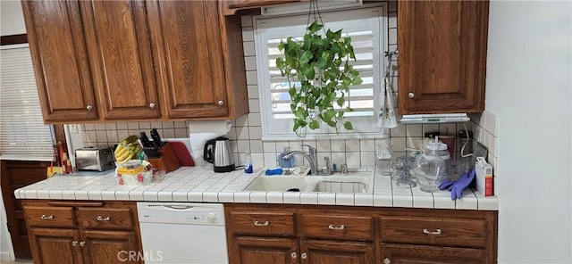 kitchen featuring sink, backsplash, dishwasher, and tile counters