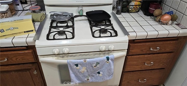 room details with tile countertops, dark brown cabinetry, and white gas range oven