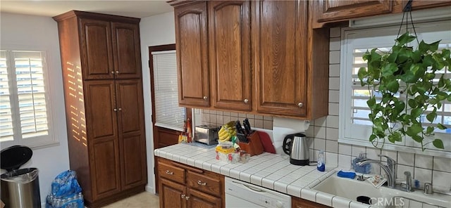 kitchen with dishwasher, tile countertops, decorative backsplash, a wealth of natural light, and sink