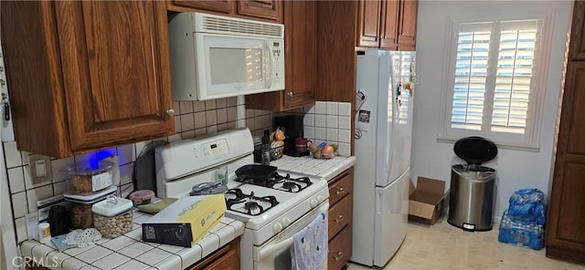 kitchen featuring tile countertops, backsplash, and white appliances