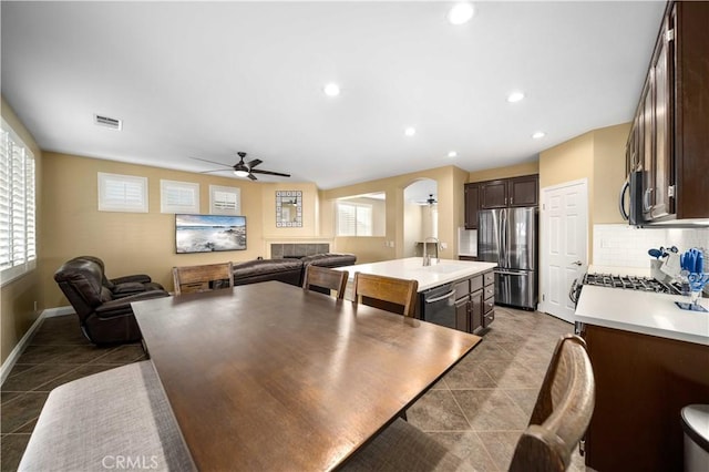 kitchen with dark brown cabinetry, appliances with stainless steel finishes, sink, ceiling fan, and a center island with sink