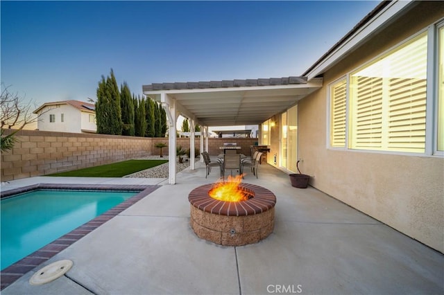 pool at dusk with an outdoor fire pit and a patio area