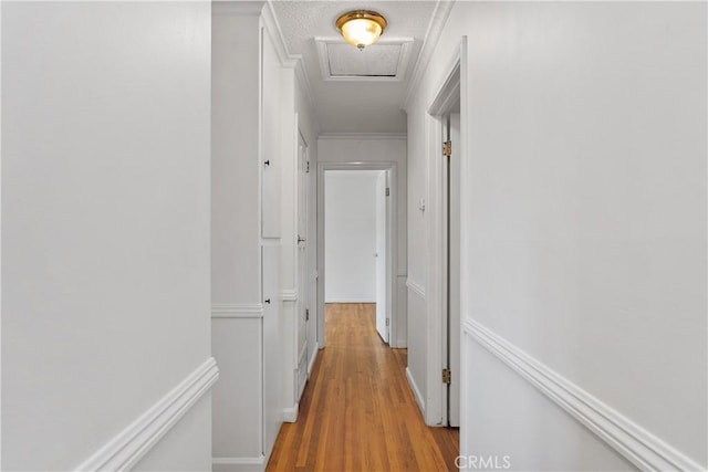 hallway featuring crown molding, a textured ceiling, and light hardwood / wood-style flooring