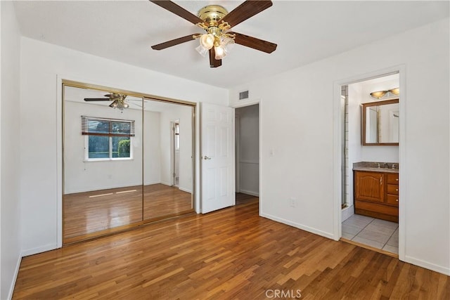 unfurnished bedroom with ceiling fan, connected bathroom, light wood-type flooring, a closet, and sink