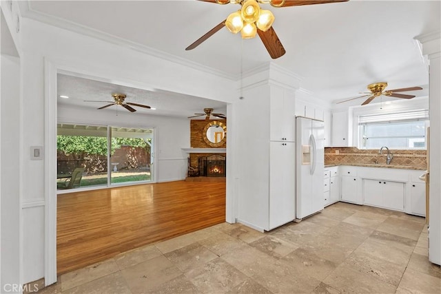 kitchen with white fridge with ice dispenser, white cabinetry, sink, a large fireplace, and crown molding