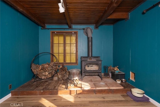 unfurnished room featuring wooden ceiling, beam ceiling, a wood stove, and hardwood / wood-style floors