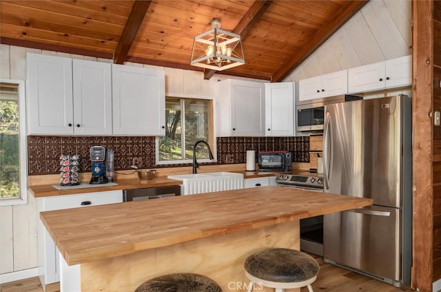 kitchen featuring white cabinetry, butcher block counters, stainless steel appliances, and vaulted ceiling with beams