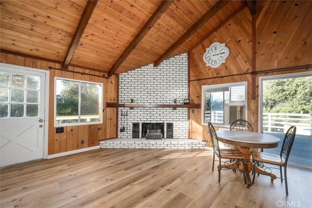 dining space with wood ceiling, wood walls, a brick fireplace, light hardwood / wood-style flooring, and beam ceiling