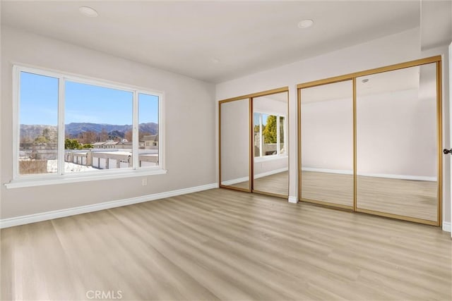 unfurnished bedroom with multiple closets, a mountain view, multiple windows, and light hardwood / wood-style floors