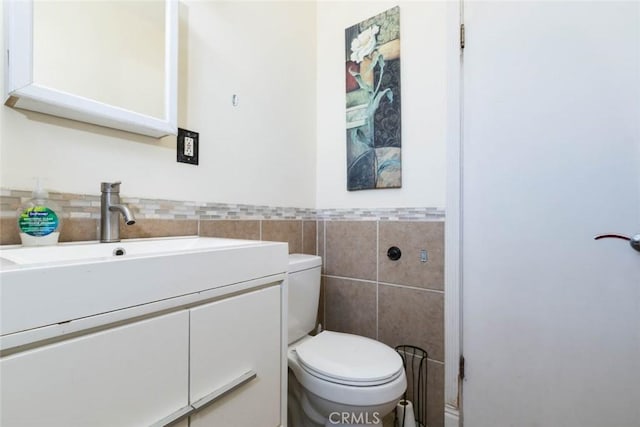 bathroom with toilet, vanity, and tile walls