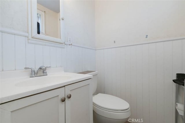 bathroom featuring toilet, vanity, and wooden walls