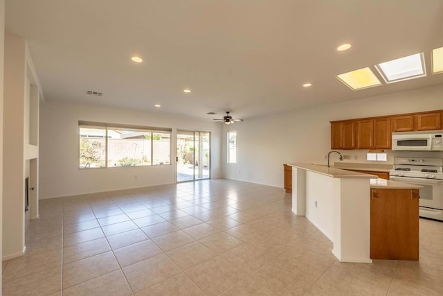 kitchen with light tile patterned floors, a center island with sink, ceiling fan, white appliances, and sink