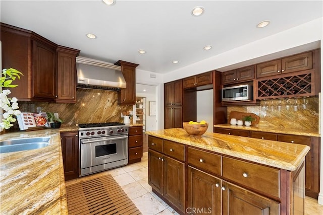 kitchen with wall chimney range hood, a center island, decorative backsplash, appliances with stainless steel finishes, and light stone counters