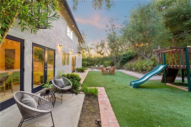 yard at dusk featuring a playground and a patio