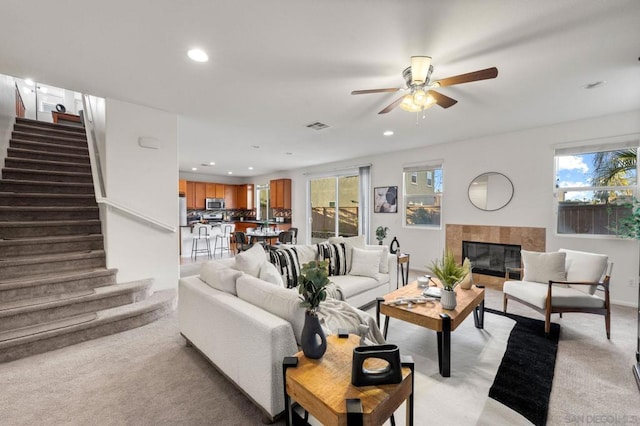 carpeted living room featuring ceiling fan, a tile fireplace, and a healthy amount of sunlight