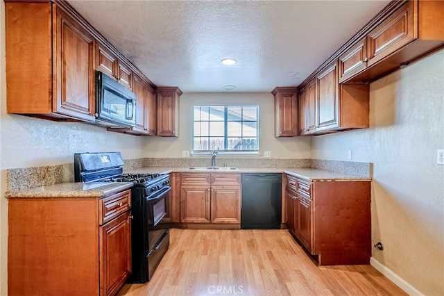 kitchen featuring a textured ceiling, black appliances, sink, light wood-type flooring, and light stone counters