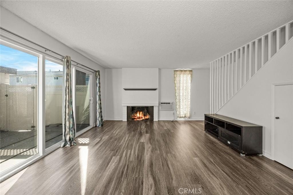 unfurnished living room with a textured ceiling, dark hardwood / wood-style flooring, and a wall mounted air conditioner