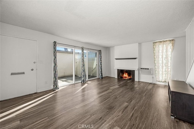 unfurnished living room with dark wood-type flooring, a textured ceiling, a wall unit AC, and a wealth of natural light