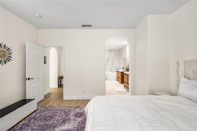 bedroom with connected bathroom and light hardwood / wood-style floors